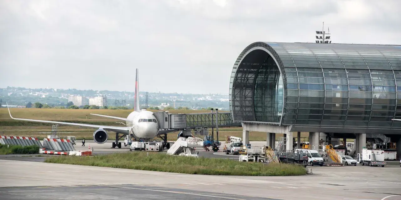 Flugzeug am Gate mit modernem Terminalgebäude. Die Frage "paris welcher flughafen am besten" wird hier nicht beantwortet, aber die Szene zeigt einen belebten Flughafen.