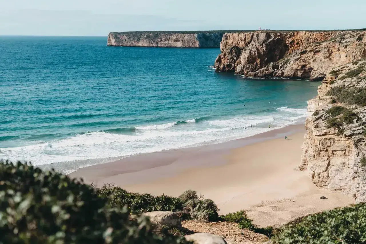 Traumhafter Strand mit Klippen und türkisfarbenem Meer. Perfekt für einen Portugal Urlaub mit Surfern im Wasser.