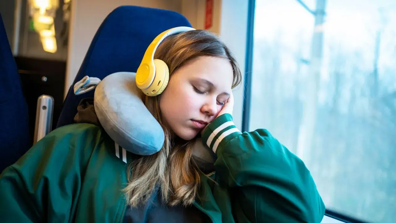 Mädchen schläft im Zug mit gelben Kopfhörern und einem Nackenkissen richtig benutzt für bequemen Halt.