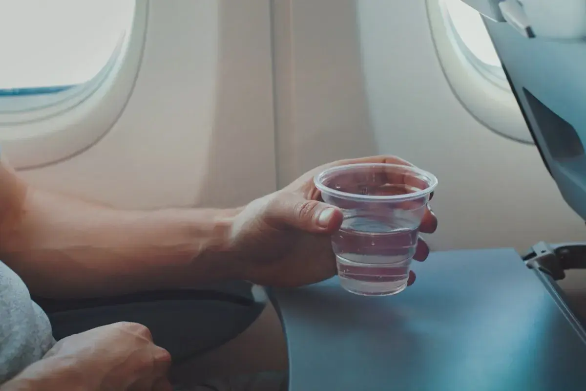 Hand hält ein Glas Wasser, während man im Flugzeug sitzt.