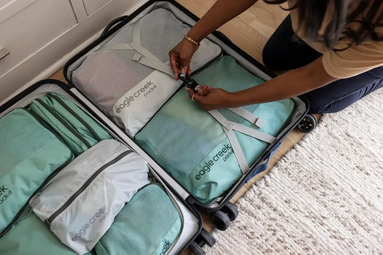Frauen packen ihre Koffer mit praktischen Reise-Must-Haves: Packwürfel in Mintgrün und Grau sortieren Kleidung für die nächste Reise.