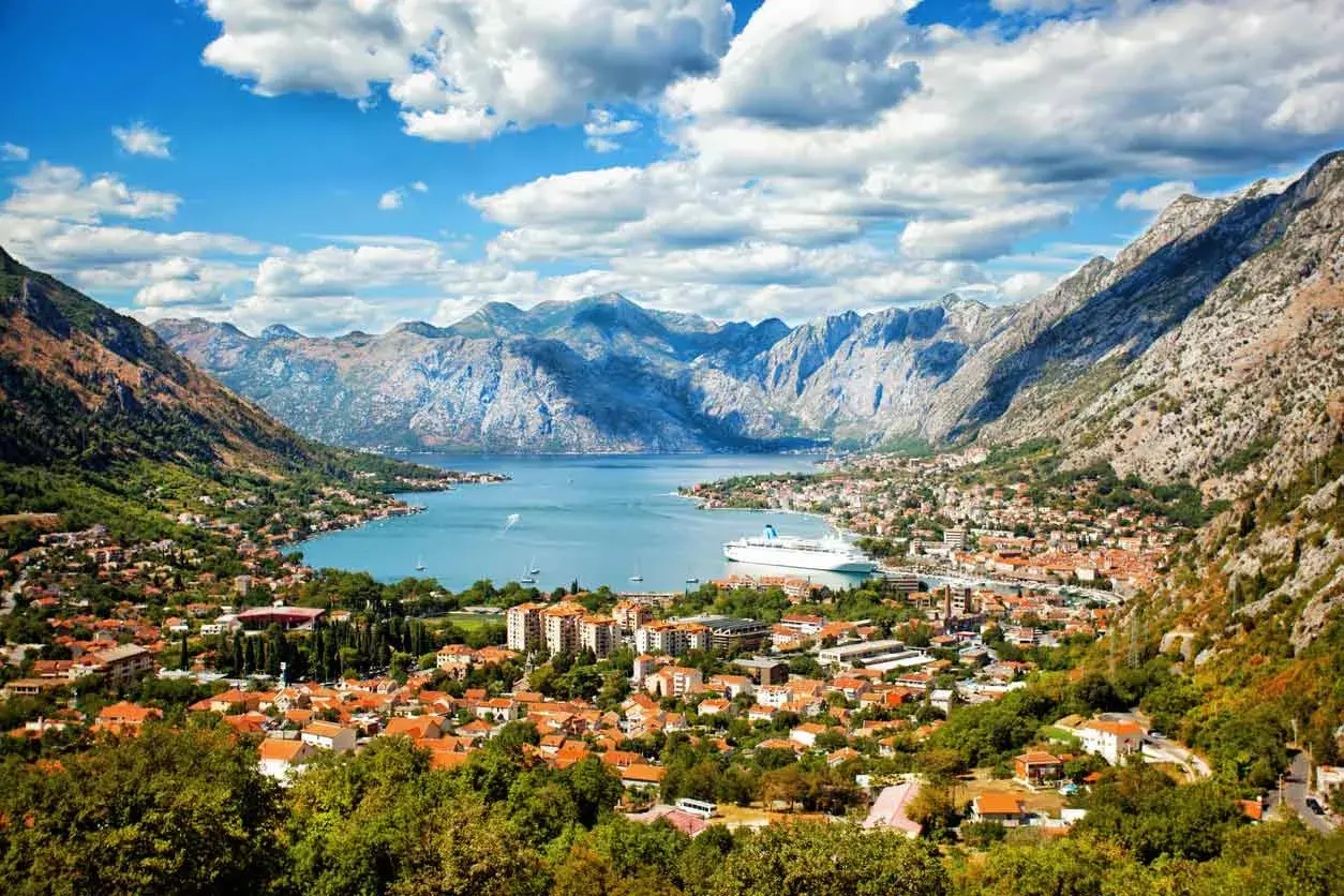 Traumhafter Urlaub in Montenegro: Die Bucht von Kotor mit Kreuzfahrtschiff und malerischer Stadt vor imposanter Bergkulisse.