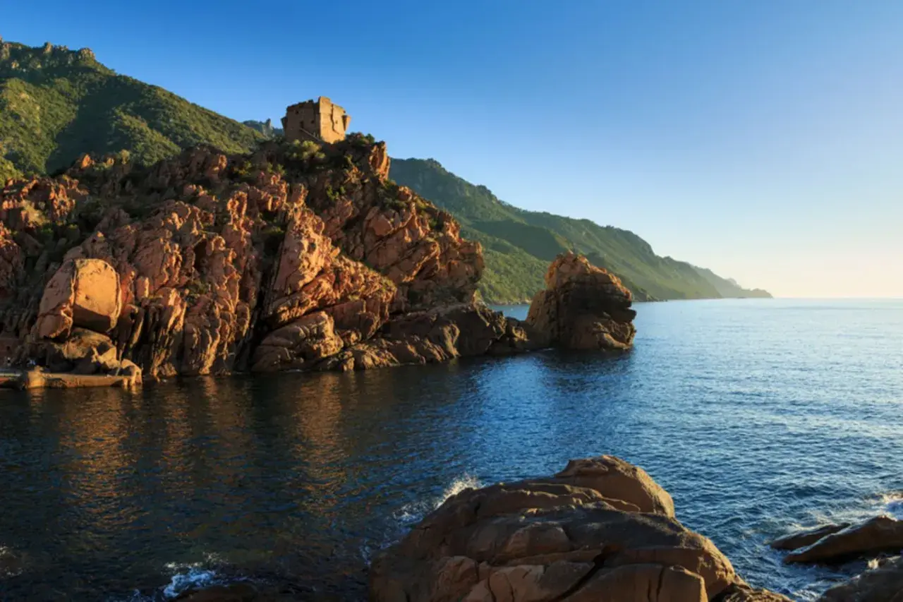 Ein alter Turm thront auf roten Felsen am Meer. Perfekt für einen Urlaub im Juli.