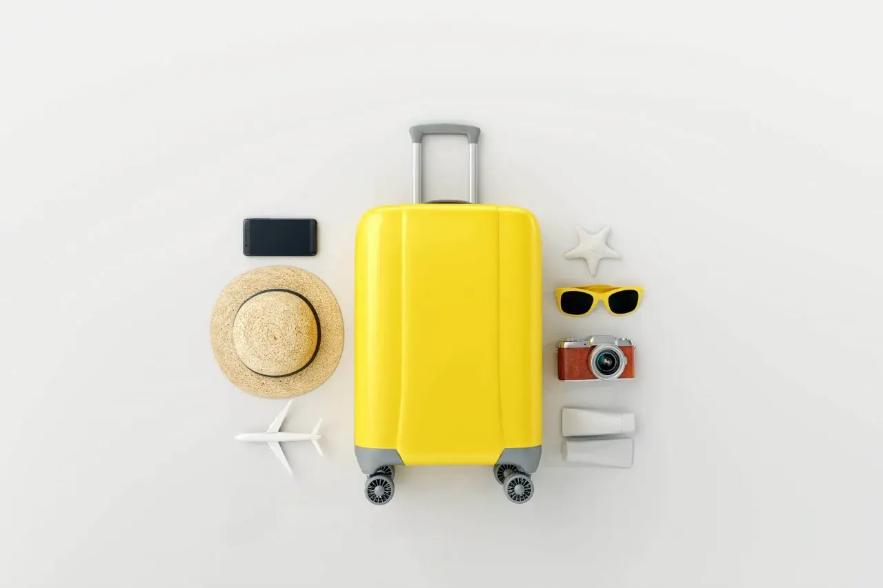 Gelbe Reisetasche mit Hut, Sonnenbrille, Kamera, Handy und Flugzeug – die perfekten roadtrip must haves für deinen Urlaub.