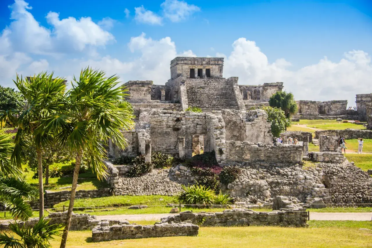 Ruinen von Tulum, ein Traumziel für jeden Mexiko Urlaub. Palmen und antike Bauten unter blauem Himmel.