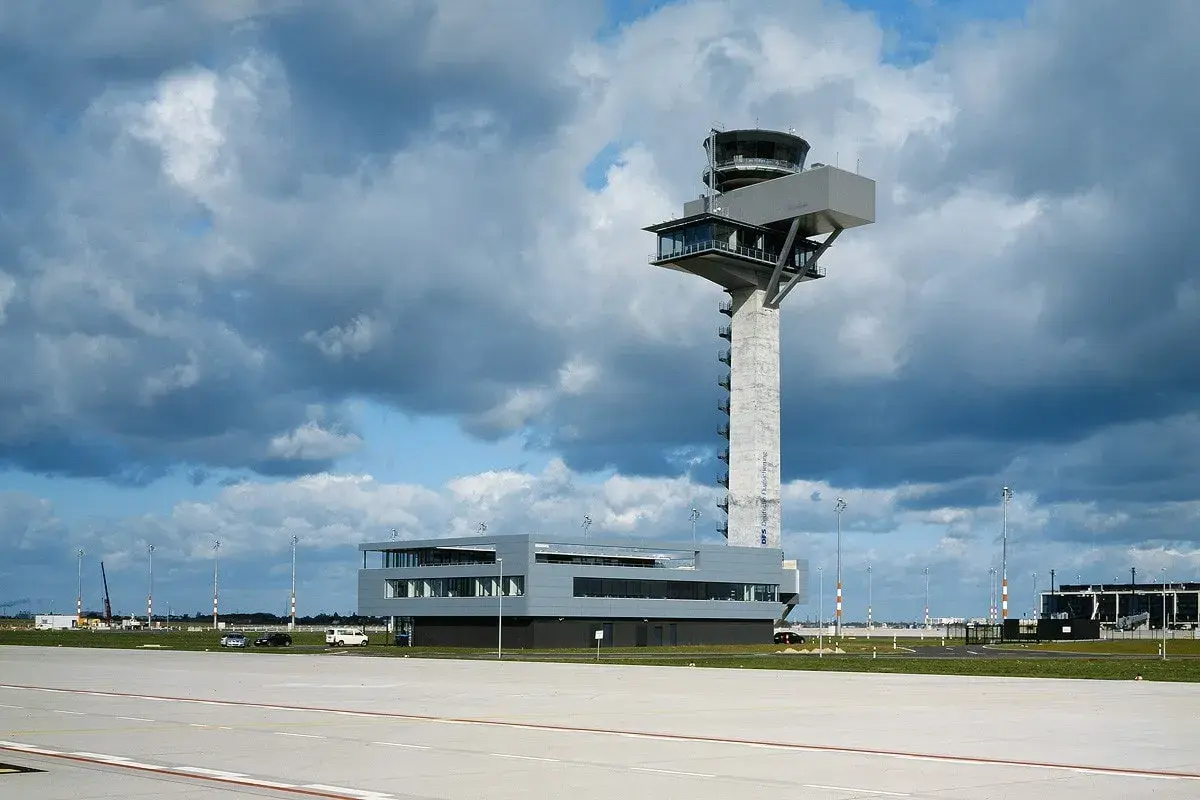 Moderner flughafen tower mit Glasfronten und einem Betonpfeiler, der über das Rollfeld ragt.