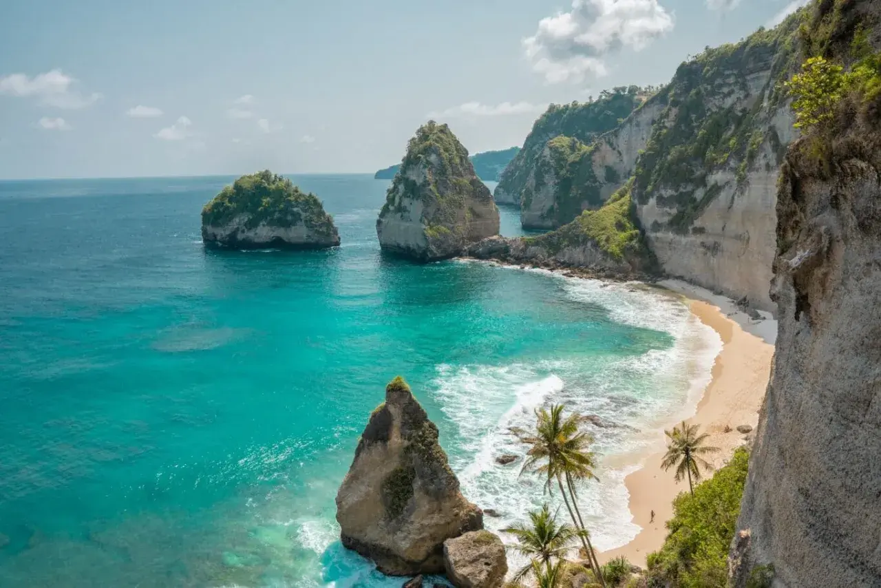 Traumhafter Urlaub auf Bali: Türkisblaues Meer trifft auf einsame Sandstrände und steile Felsklippen mit Palmen. Ein Paradies!