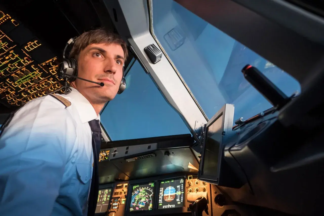 Ein Pilot im Cockpit, der aufmerksam auf die Instrumente blickt. Er trägt Kopfhörer und eine Uniform, wie ein deadhead pilot, der auf seinen Einsatz wartet.