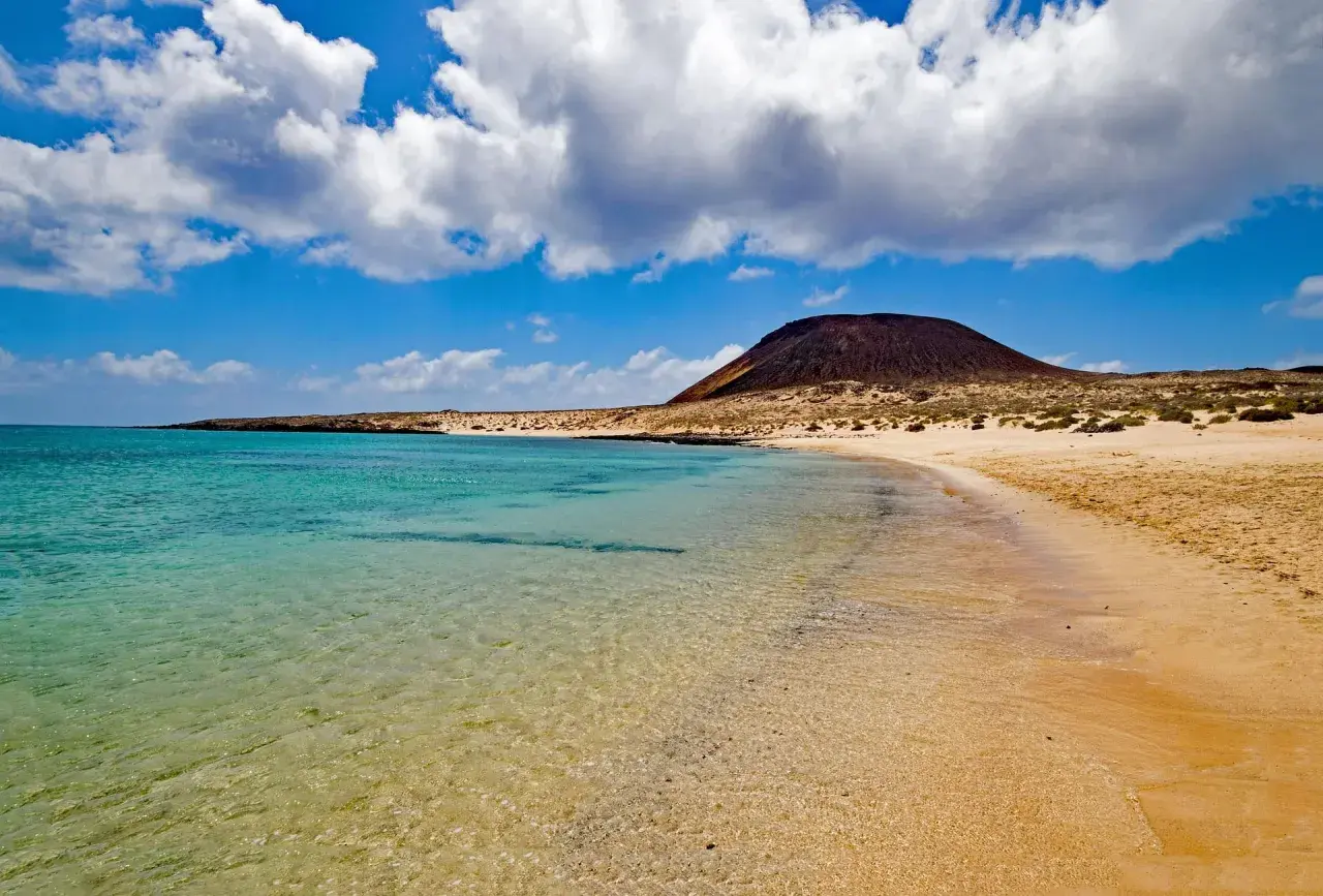 Traumhafter Strand mit türkisfarbenem Wasser und einem Vulkan im Hintergrund – ideal für Ihren Kanaren Urlaub.