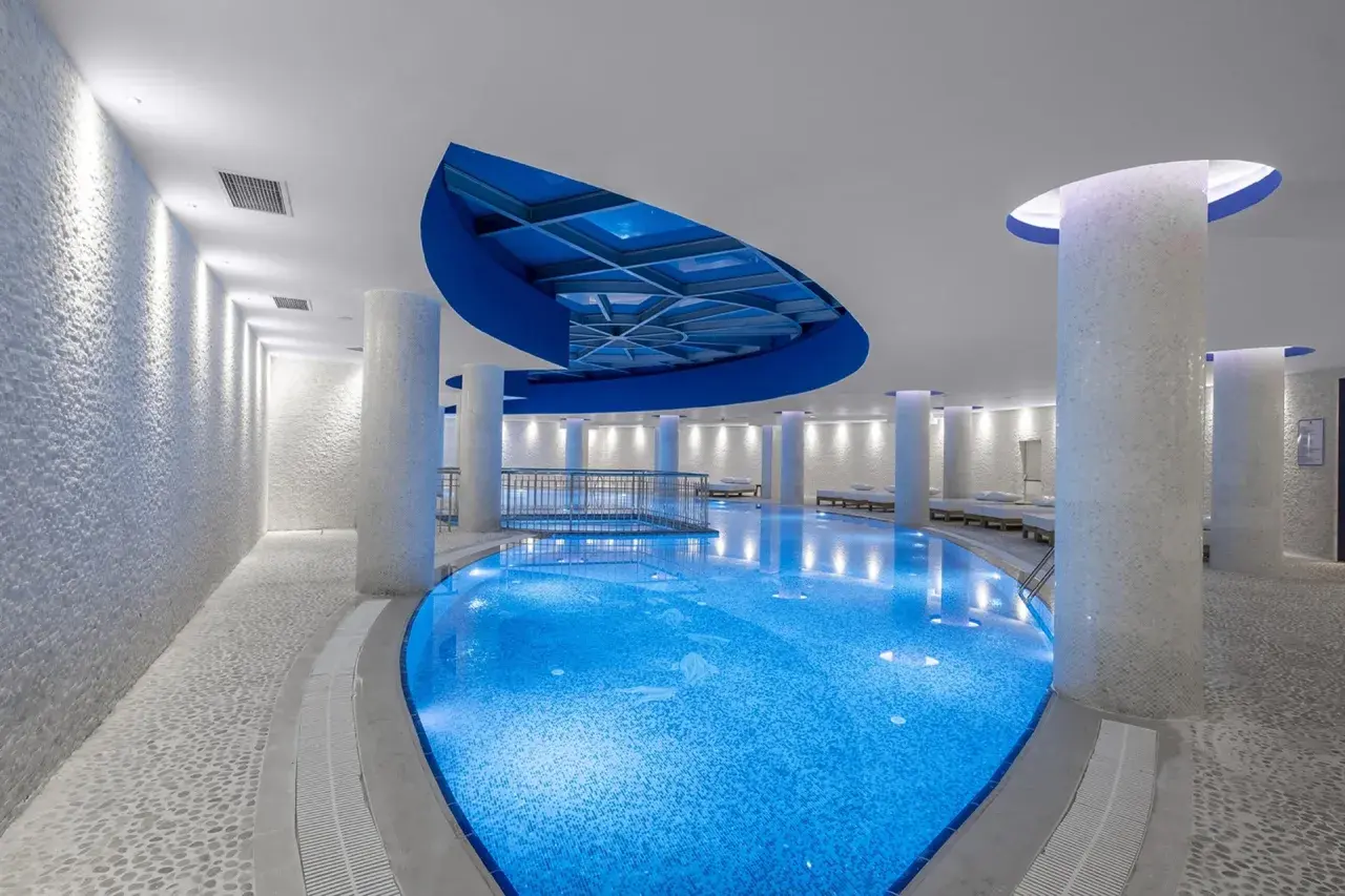 Ein luxuriöses Schwimmbad mit blau beleuchtetem Wasser, umgeben von weißen Säulen und Mosaikwänden. Ein Ort, der wie ein **rubi platinum sign** für Entspannung wirkt.