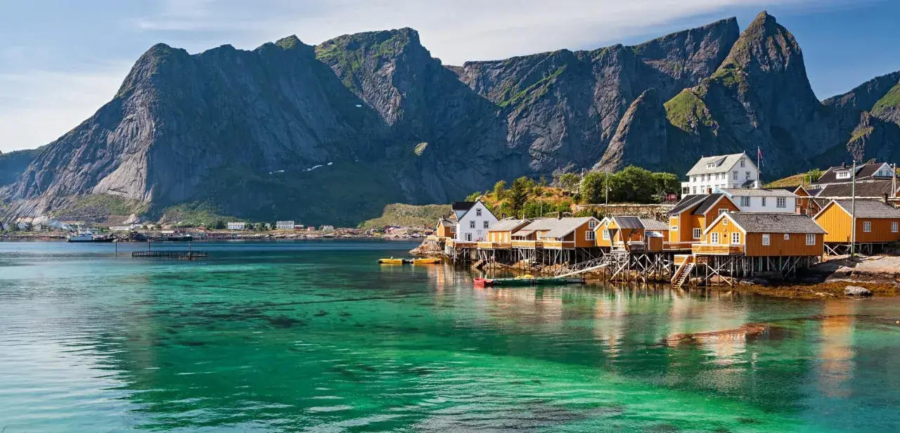Idyllische Fischerhäuser auf Stelzen am kristallklaren Wasser vor majestätischen Bergen. Ein perfekter Urlaub in Norwegen.