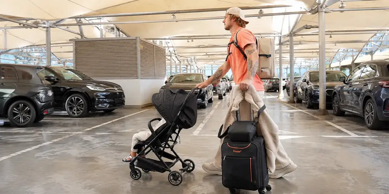 Mann mit Gepäck und Kinderwagen auf dem Parkplatz eines Flughafens.