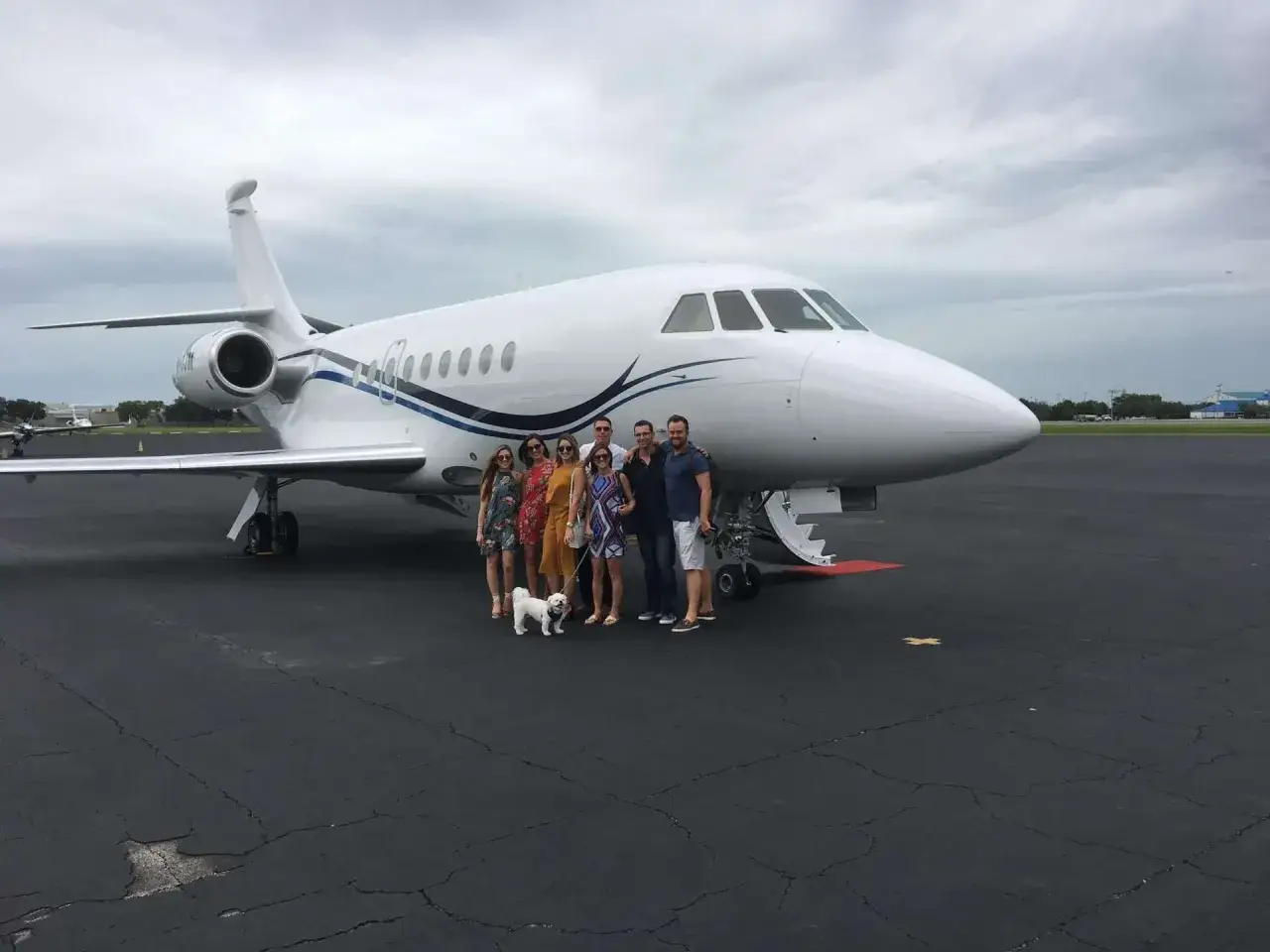 Gruppe von Freunden und ein Hund stehen vor einem Privatjet, bereit, in die Luft zu steigen.