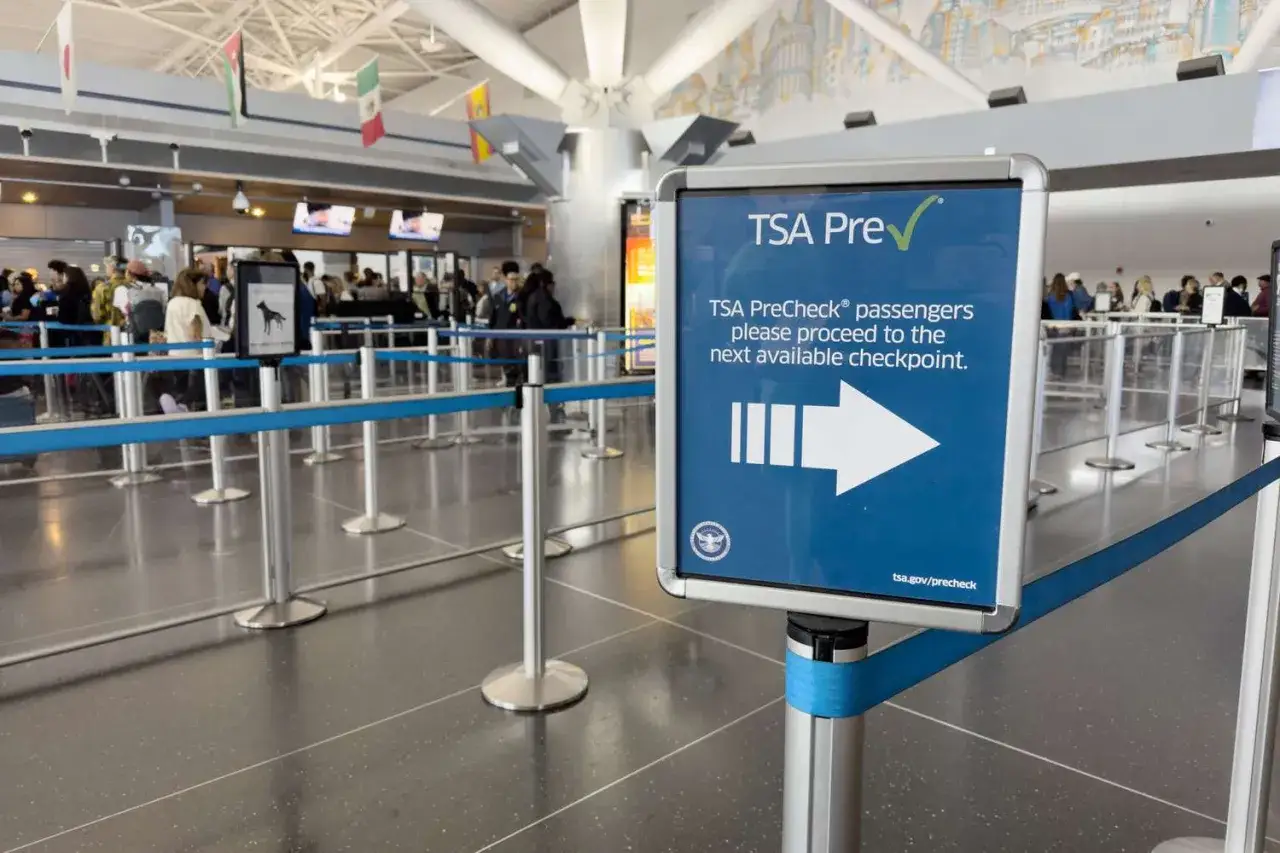 Schild bei der flughafen sicherheitskontrolle weist TSA PreCheck-Passagieren den Weg. Menschen stehen in der Schlange.