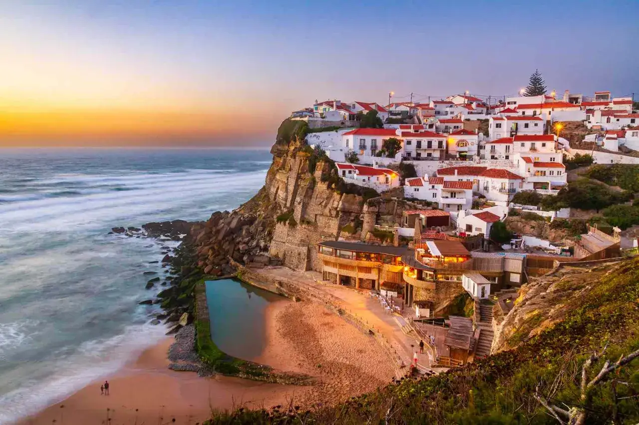 Traumhafter Urlaub in Portugal am Meer: Weiß getünchte Häuser mit roten Dächern thronen auf einer Klippe über dem Atlantik. Ein idyllischer Strand mit einem Pool lädt zum Entspannen ein.