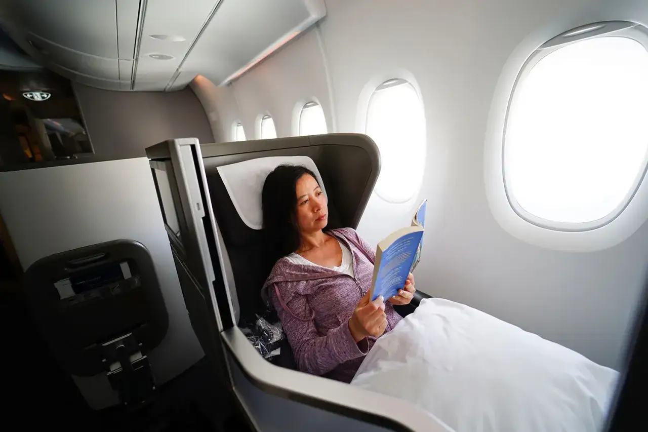 Frau liest Buch im Flugzeugsitz. Gute tipps langstreckenflug: Bequemlichkeit und Ablenkung sind wichtig.