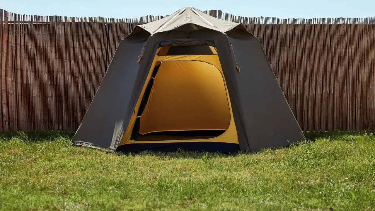 Ein Zelt steht auf einer grünen Wiese vor einem Bambuszaun. Perfekt für die Parookaville Packliste!