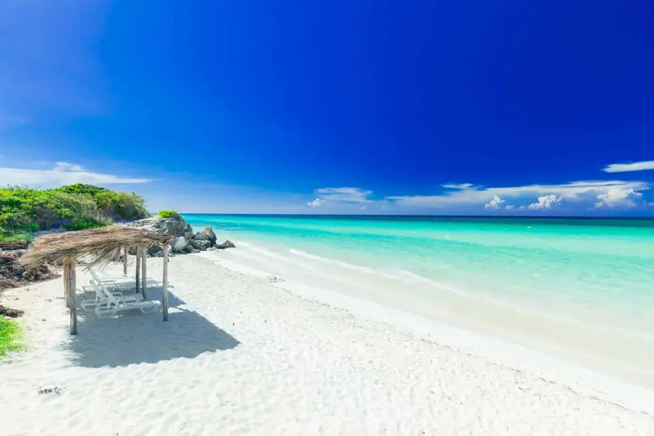 Traumhafter Strand mit Palmenhütte und Liegen. Türkises Meer und blauer Himmel – die beste Reisezeit Kuba für pure Entspannung.