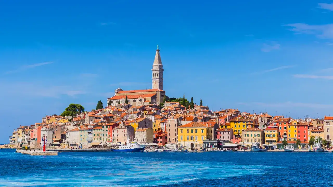 Bunte Häuserfront am Meer, ein Kirchturm ragt empor. Perfekt für einen Kurztrip Europa.