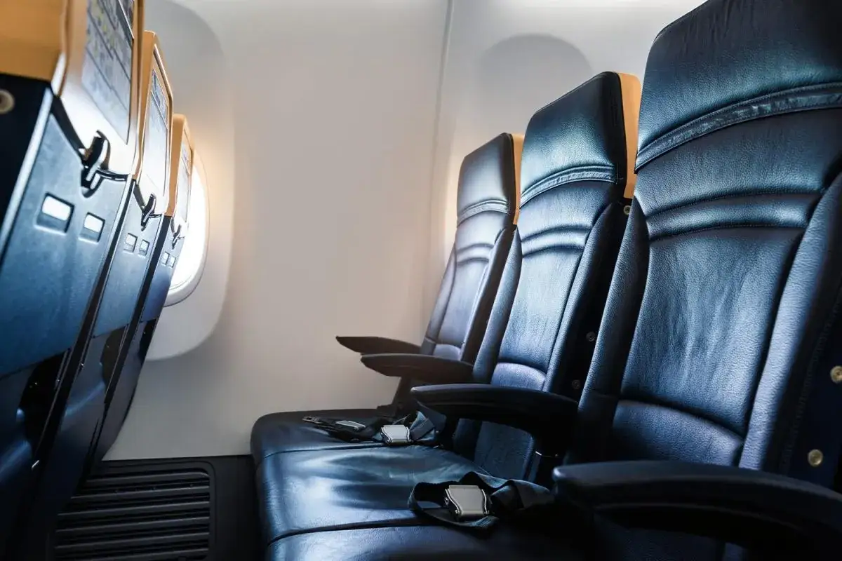Reihe von schwarzen Ledersitzen im Flugzeug, mit Gurten und Armlehnen. Ein Fenster wirft warmes Licht auf den Sitzplatz a im Flugzeug.