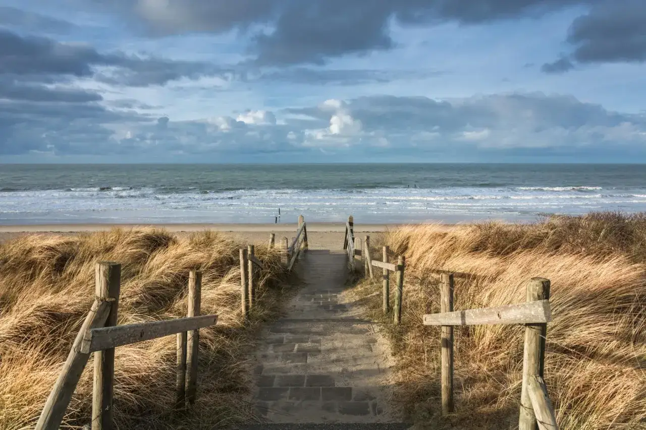 Treppe durch Dünen zum Meer. Ein perfekter Ort für einen Urlaub in Holland am Meer, mit Wellen und weitem Himmel.