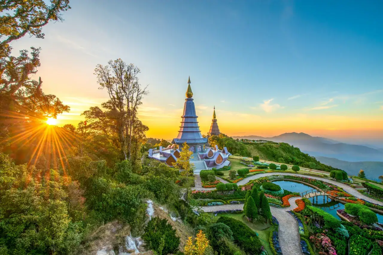 Sonnenaufgang über Doi Inthanon, Chiang Mai. Zwei goldene Pagoden thronen über einem blühenden Garten mit einem Teich und einer Brücke.