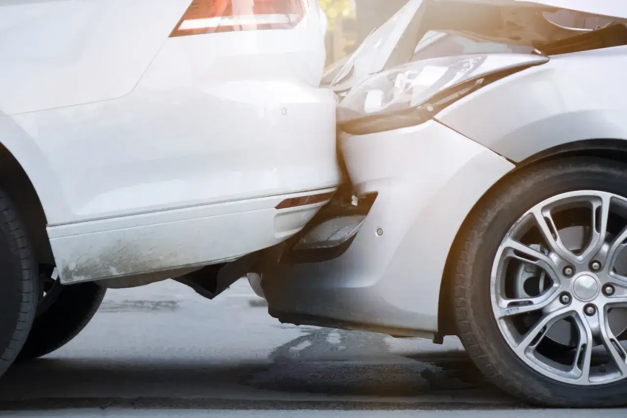 Zwei Autos sind kollidiert, ein weißes und ein silbernes. Der Schaden deutet auf einen unglücklichen Unfall beim Ausparken hin.