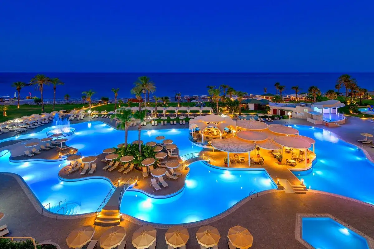 Ein beleuchteter Poolbereich mit Palmen und Liegestühlen am Abend. Das Lindos Princess Beach Hotel lädt zum Entspannen ein.
