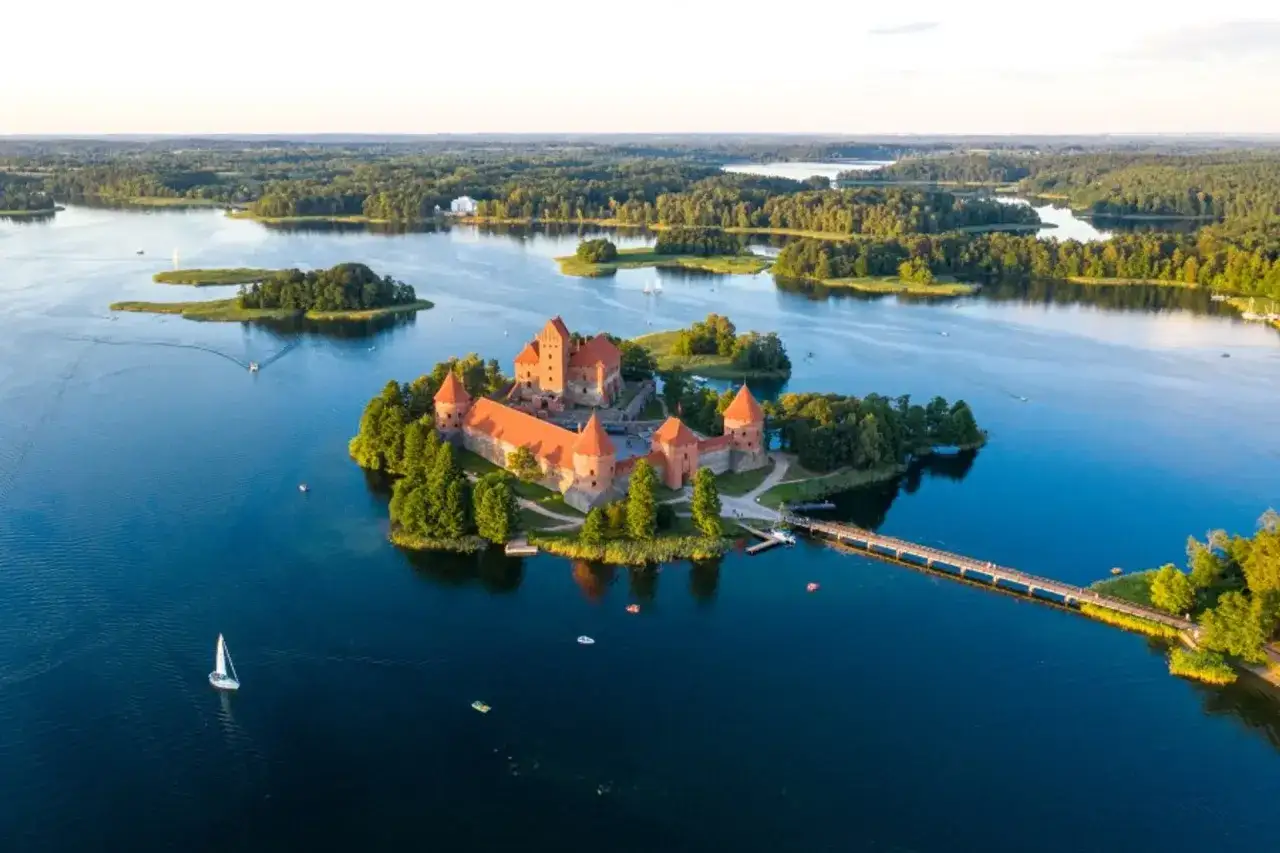 Traumhafter Litauen Urlaub: Trakai Burg auf einer Insel im See, umgeben von Wäldern. Ein Segelboot gleitet über das Wasser.