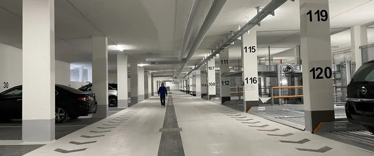 Ein Mann geht durch eine moderne Tiefgarage mit nummerierten Stellplätzen, die auf Parkplatz-Sharing-Systeme hindeuten.