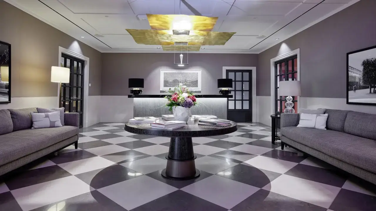 Elegante priority lounge mit Schachbrettboden, zwei Sofas, einem runden Tisch mit Blumen und Büchern sowie einer Rezeption.