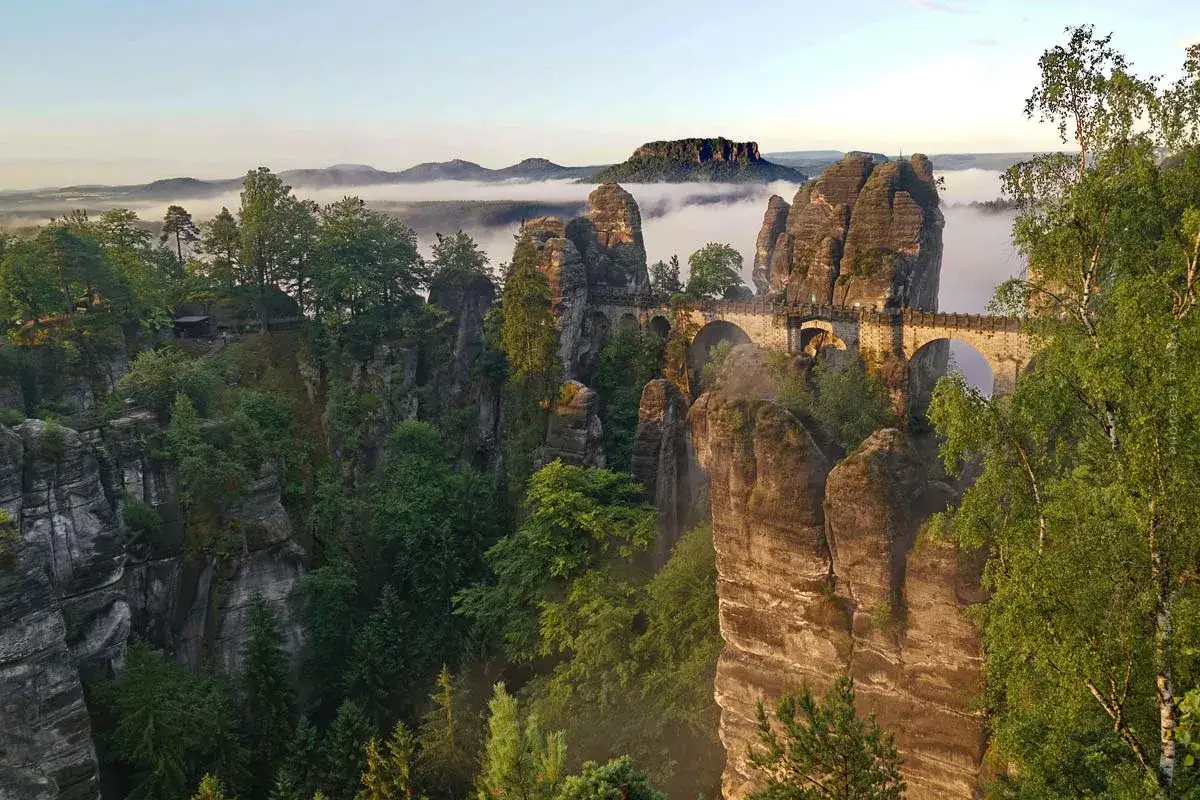 Morgendlicher Nebel über Felsen und Wäldern, eine Brücke verbindet Gipfel. Perfekt für einen outdoor urlaub.