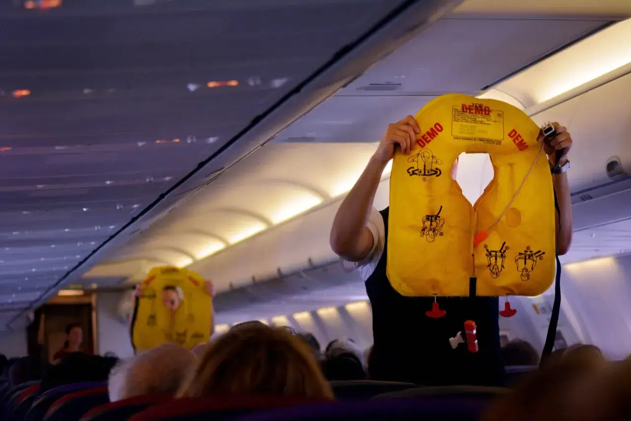 Flugzeug Ansage Text Deutsch: Crew demonstriert Schwimmwesten. Gelbe Westen mit Anleitungen sind sichtbar.