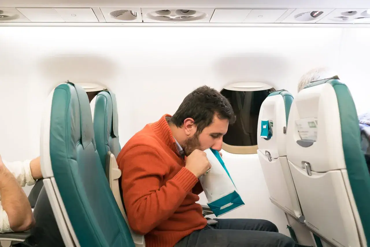 Mann im Flugzeug mit Tüte gegen Reisekrankheit.