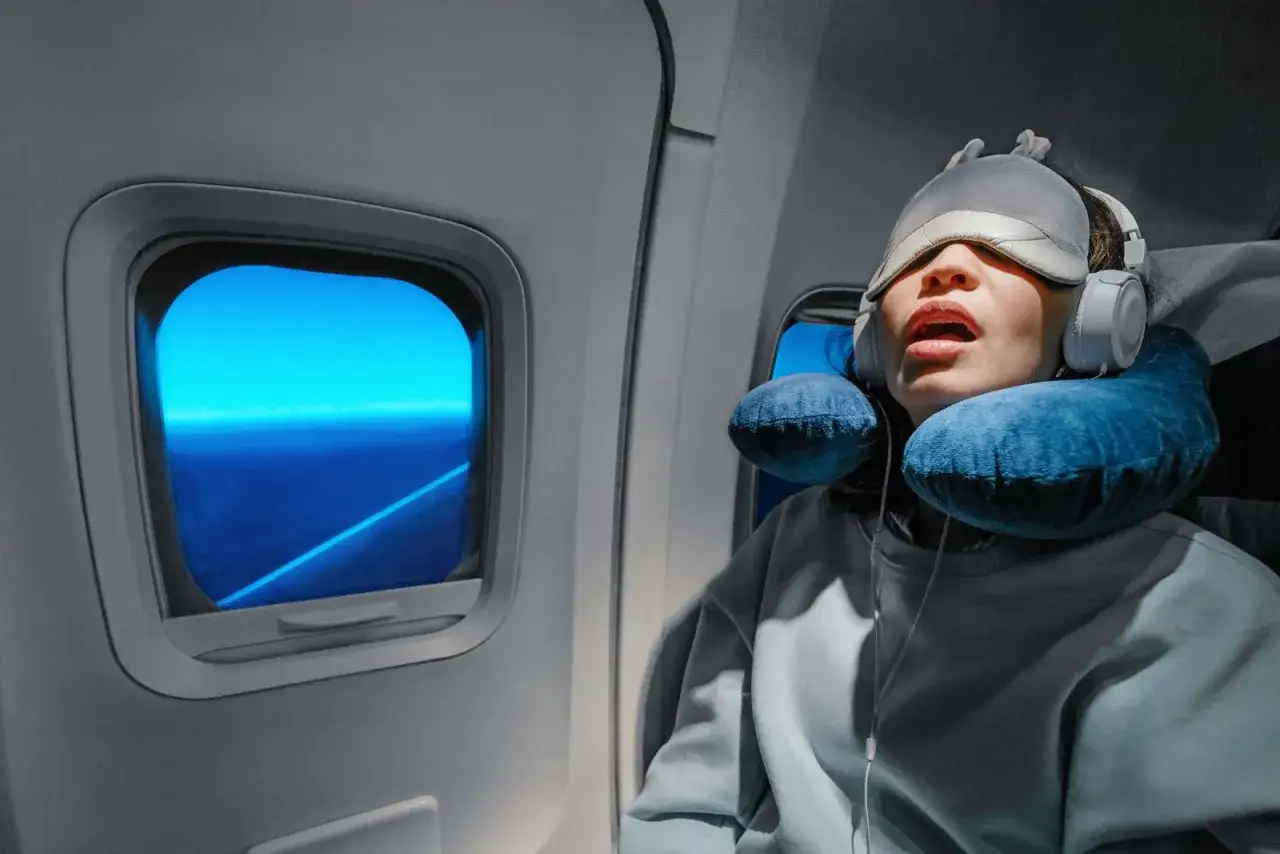 Müde Reisende im Flugzeug, kämpft mit Jetlag von Asien nach Deutschland, mit Schlafmaske und Nackenkissen.