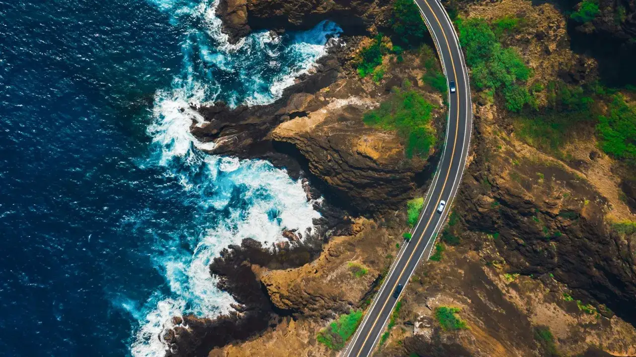 Traumhafte Küstenstraße mit dem Auto ans Mittelmeer. Wellen brechen an Felsen, grüne Hänge säumen die Straße.