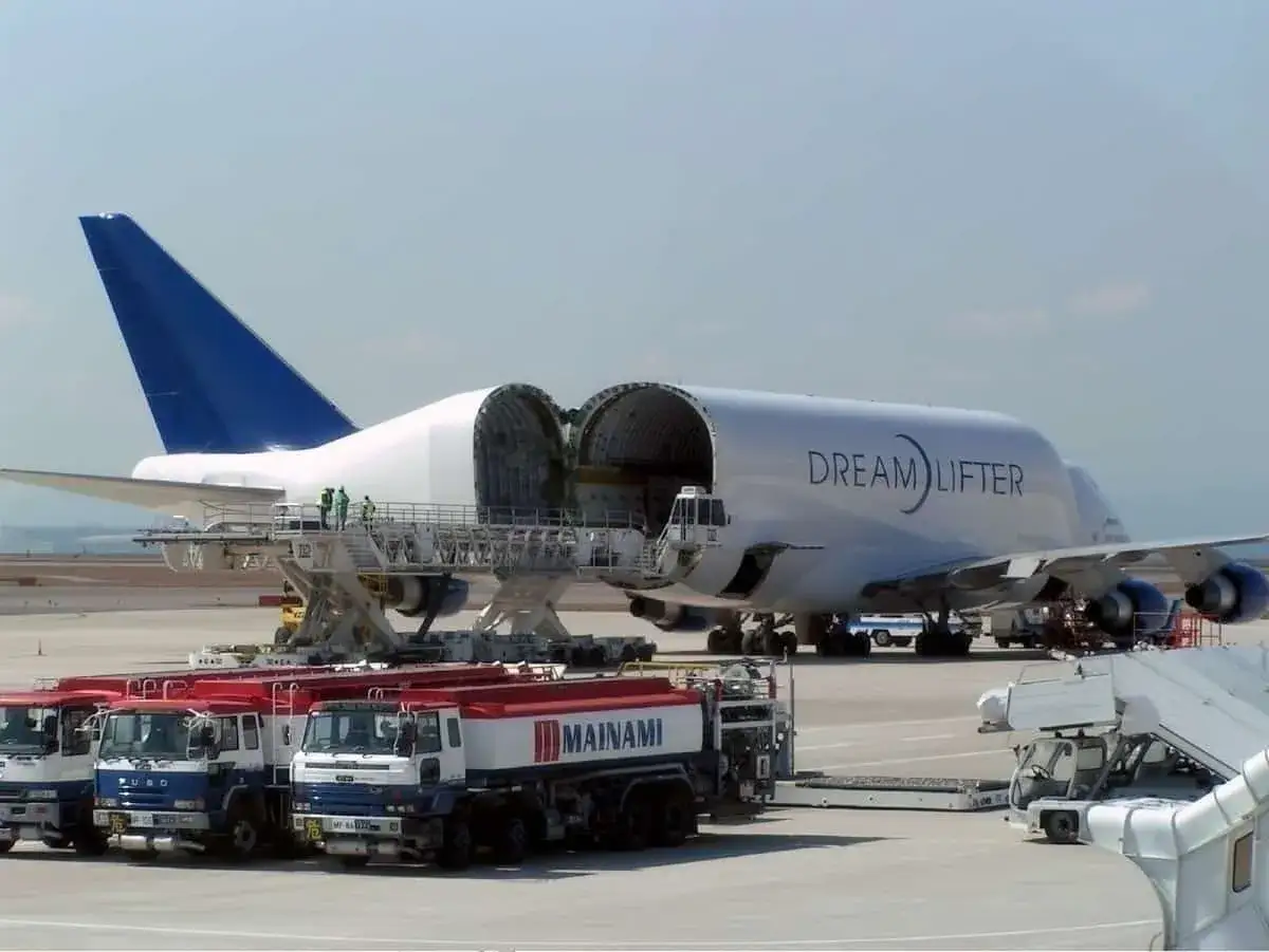 Der Dreamlifter mit geöffnetem Rumpf steht bereit. Mehrere Tankwagen warten auf dem Rollfeld.