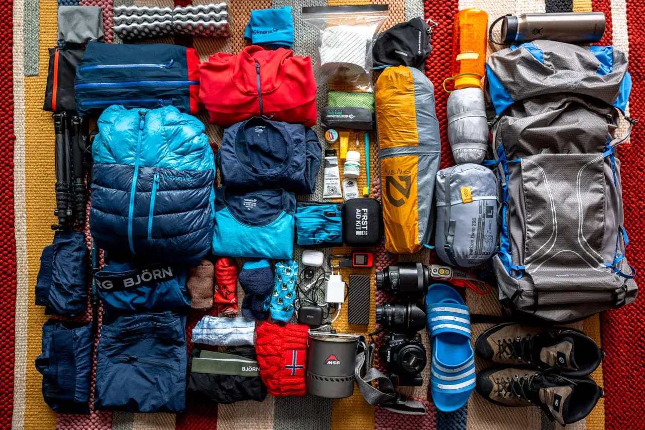 Packliste Norwegen: Daunenjacke, Rucksack, Wanderschuhe, Kocher, Kamera, Erste-Hilfe-Set und Kleidung für Outdoor-Abenteuer.