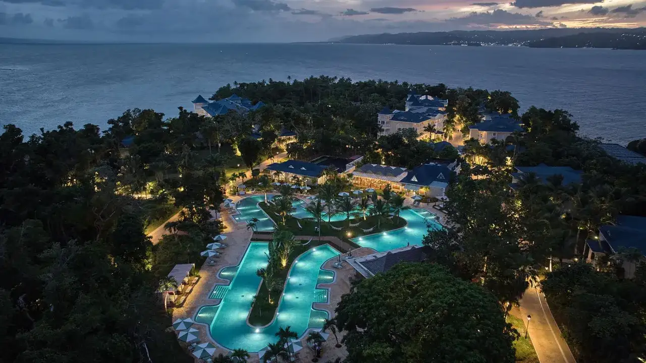 Traumhafter Dominikanische Republik Urlaub: Ein Resort mit beleuchteten Pools und tropischer Vegetation am Meer bei Dämmerung.