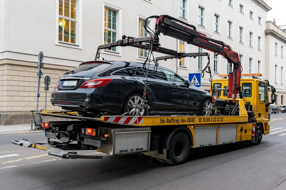 Ein schwarzer Kombi wird von einem gelben Abschleppwagen auf einem Parkplatz in der Stadt transportiert. Die Kosten für eine Leerfahrt des Abschleppdienstes können variieren.