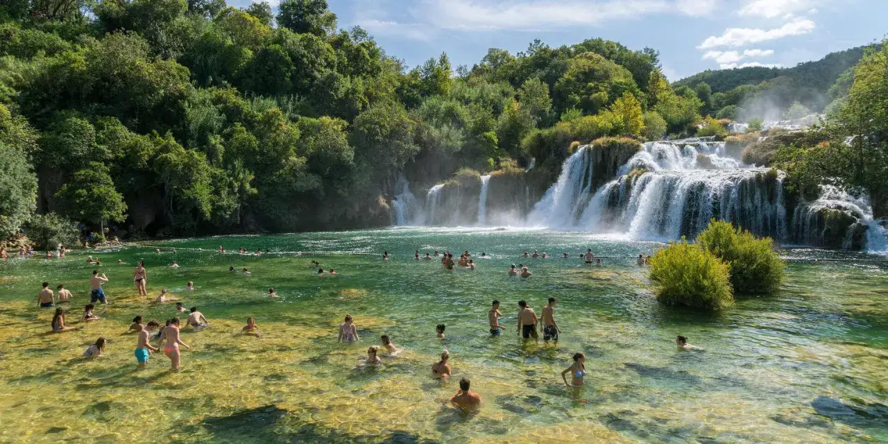 Erfrischende Wasserf&auml;lle in Krka Nationalpark, Kroatien. Menschen baden im kristallklaren Wasser vor &uuml;ppiger Vegetation. Ein idyllischer Ort nahe Split, Kroatien.