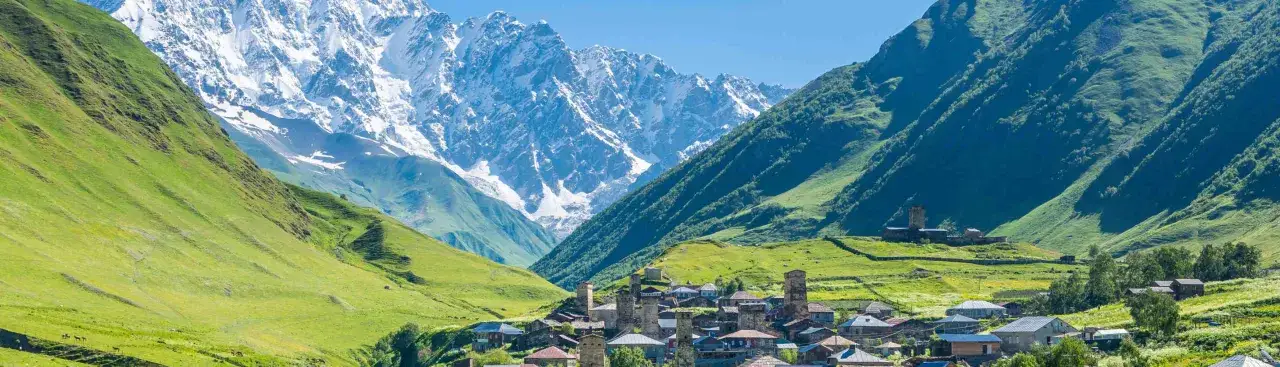 Ein malerisches Dorf in Georgien, eingebettet in grüne Täler mit schneebedeckten Bergen im Hintergrund. Perfekt für einen unvergesslichen Georgien Urlaub.