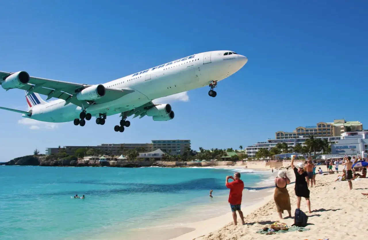 Air France Flugzeug landet tief über Maho Beach Flughafen. Touristen am Strand fotografieren das Spektakel.