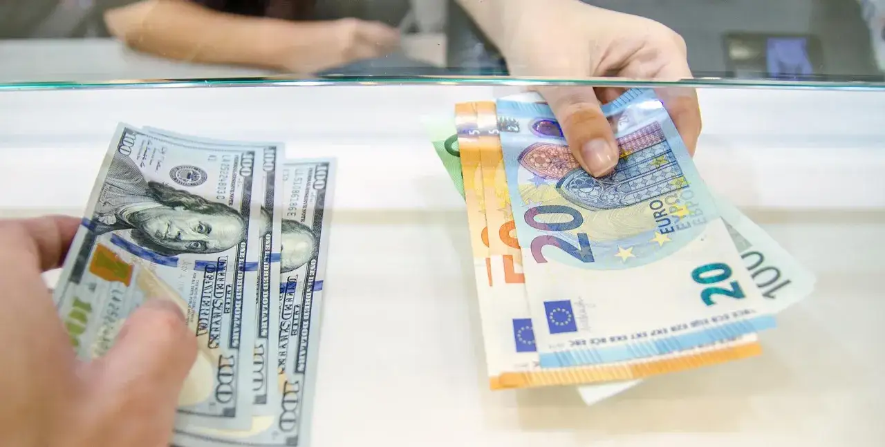 Hände tauschen Dollar- und Euroscheine über einen Tresen. Hier kann man bei der Bank Geld wechseln.