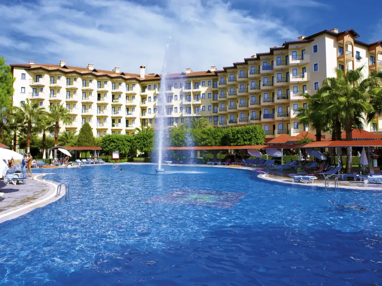 Einladender Poolbereich mit Wasserrutsche und Sonnenschirmen vor dem Miramare Queen Hotel.