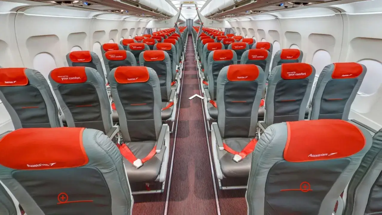 Blick in den Gang eines Airbus A320 innen mit roten und grauen Sitzen, bereit für Passagiere.
