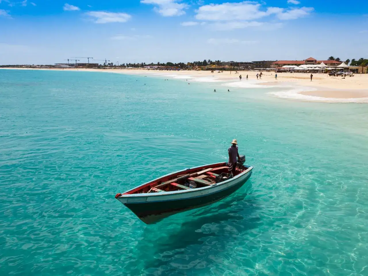 Ein Fischer steht in seinem Boot vor der Küste von Kap Verde. Türkises Wasser und ein sonniger Strand im Hintergrund.