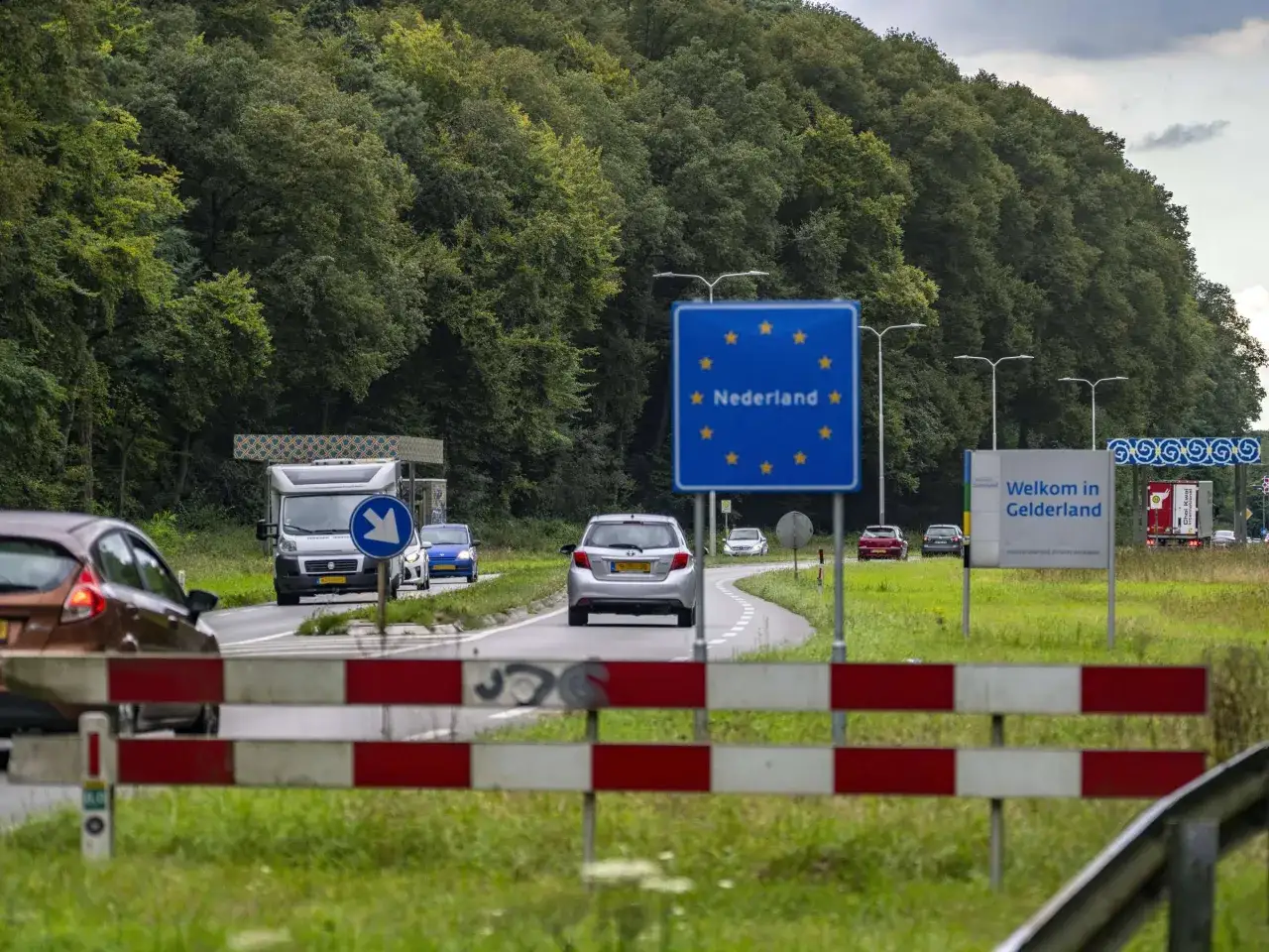 Autos nähern sich der Grenze. Ein Schild zeigt 