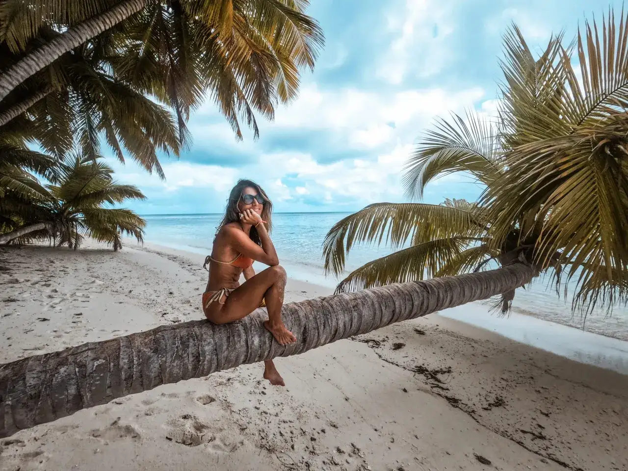 Traumhafter Urlaub in Afrika: Frau sitzt auf einer Palme am Strand, das Meer im Hintergrund.