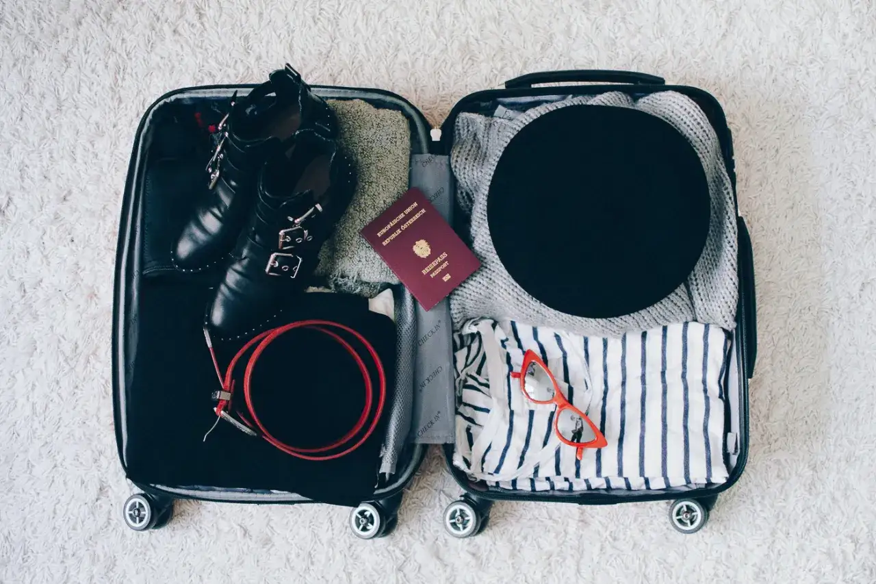 Packliste Paris: Schwarze Stiefel, ein Hut, gestreifte Kleidung, ein Reisepass und rote Brille sind bereit für die Reise.